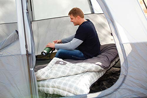 Man sitting in a tent with sleeping bags, holding a thermos.